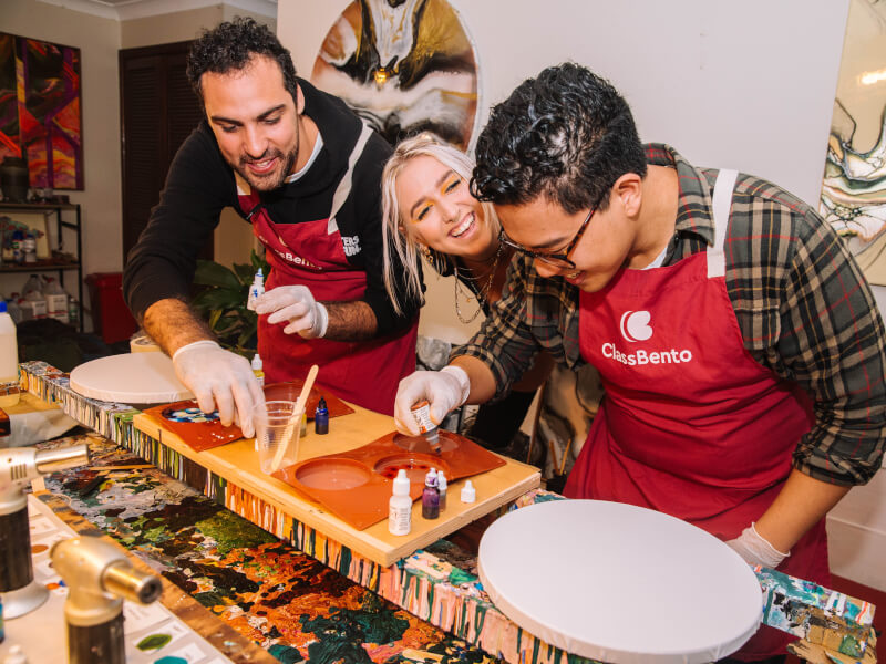 A woman laughing in-between two men wearing aprons making fluid art.